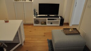Ett vardagsrum med en platt-TV, ett vitt skåp, ett litet bord och en grå soffa.