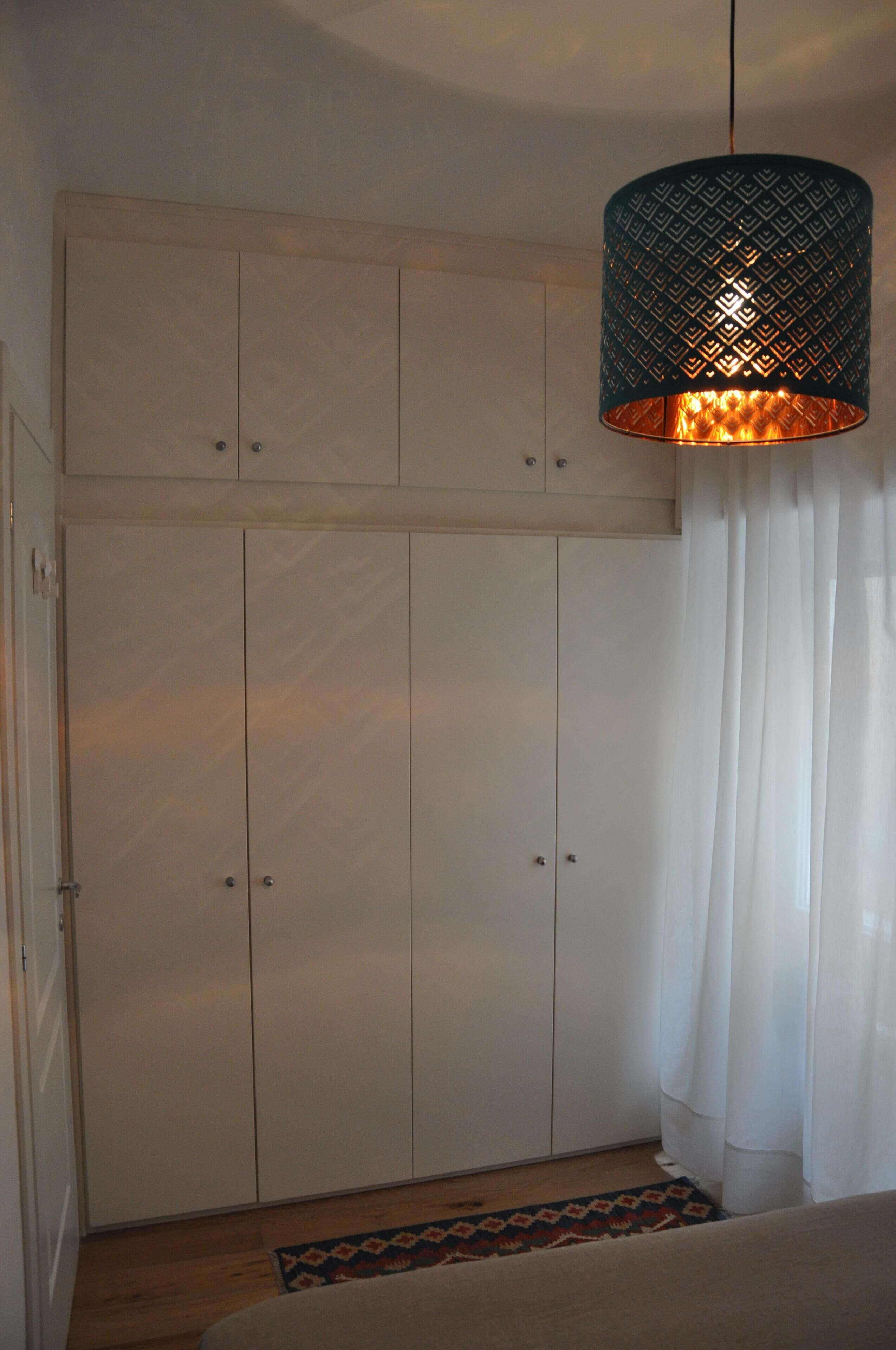 A room with a wardrobe, a hanging light fixture, and a patterned rug.
