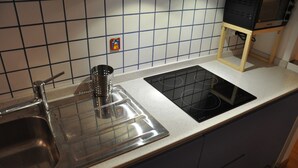 Ett kök med en diskho i rostfritt stål, en svart spis och ett litet fönster med en färgglad dekoration.