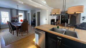 Une cuisine moderne avec un plan de travail en bois, des meubles noirs et un grand évier. On y trouve un coin repas avec une table et des chaises, et une cheminée en arrière-plan.