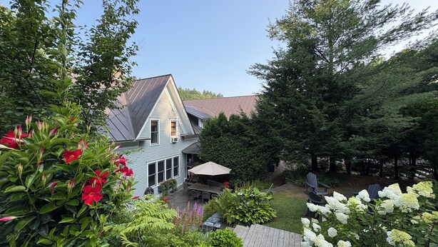 Une maison avec un toit en pente, une terrasse et un jardin où poussent différentes plantes et fleurs.