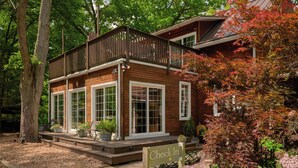 A two-story wooden house with a balcony, large windows, and a 'Check In' sign.