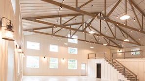 A spacious interior with high ceilings, exposed wooden beams, and a staircase leading to an upper level.