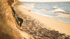 A person sitting on a sandy beach with waves in the background.