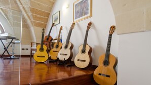 A room with a wooden floor, a piano, and several acoustic guitars leaning against the wall.