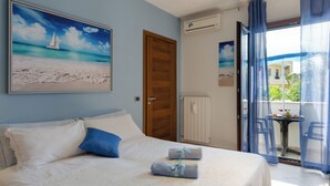 A bedroom with a bed, pillows, a painting of a beach scene, an air conditioning unit, and a view through a window with curtains.