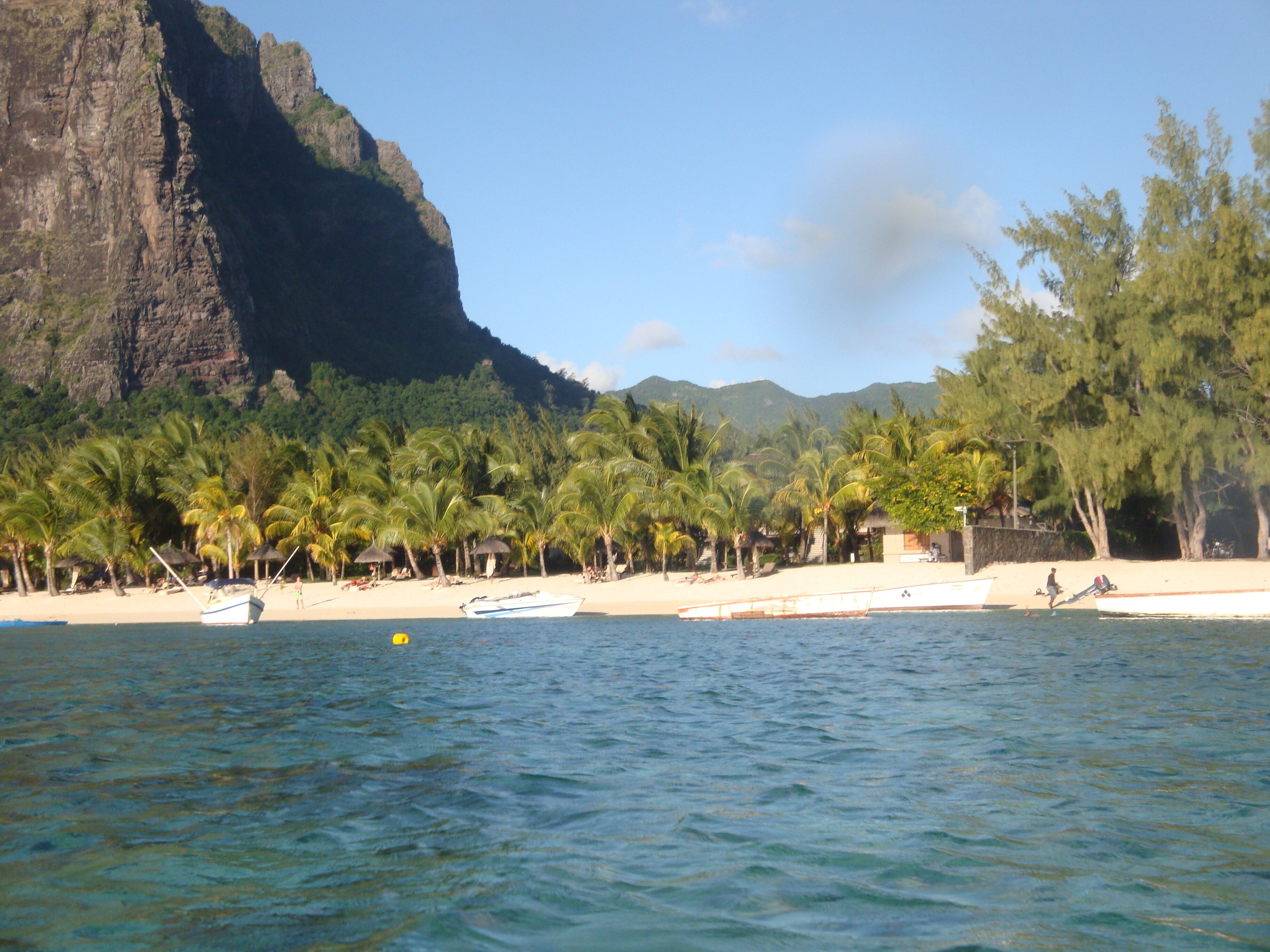 Ein Strand mit Palmen, einem Boot und einem Berg im Hintergrund.