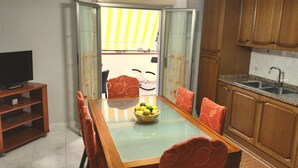 Ein Essbereich mit einem Tisch mit Glasplatte, orangefarbenen Stühlen, einer Obstschale und einem Fernseher auf einem Schrank.