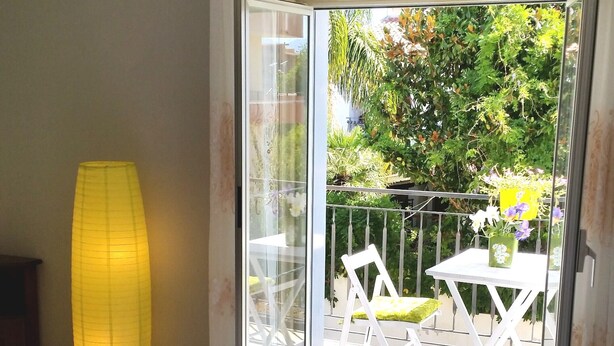 Ein Zimmer mit einem Bett, einer gelben Lampe und einer Glastür, die zu einem Außenbereich mit Tisch und Stühlen führt.