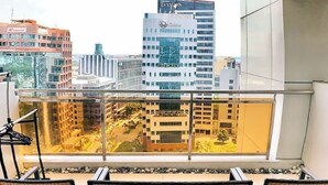 Un balcón con sillas de mimbre, barandilla de vidrio y vistas a edificios urbanos, incluyendo un hotel Globe.