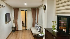 Una sala de estar con sofá, televisión, piso de madera y ventana con cortinas.