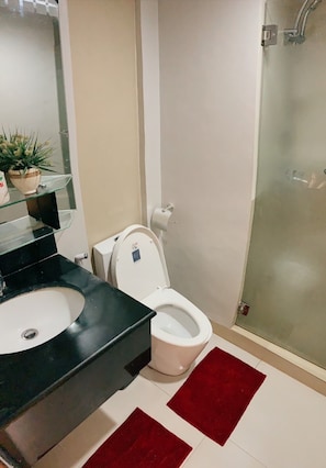 Ein Badezimmer mit Toilette in Weiß, einem schwarzen Waschbecken und einer Duschkabine aus Glas.