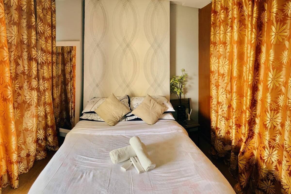 Une chambre d’hôtel avec un lit, des oreillers, une table de chevet et des rideaux.