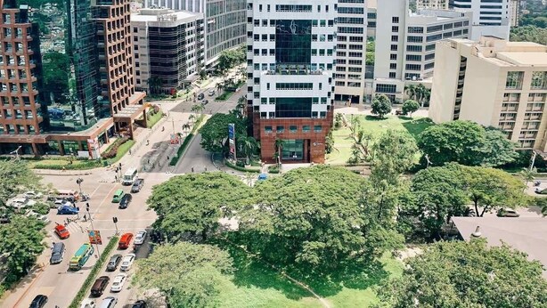 Un moderno edificio de gran altura con fachada de vidrio, rodeado de otros edificios y vegetación.