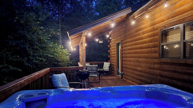 Une cabane en bois avec un jacuzzi sur la terrasse, entourée d’arbres.