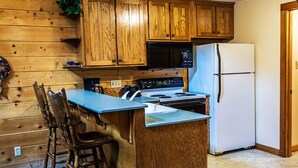 Une cuisine avec des meubles de rangement en bois, un four à micro-ondes, une cuisinière, un réfrigérateur et un plan de travail bleu.
