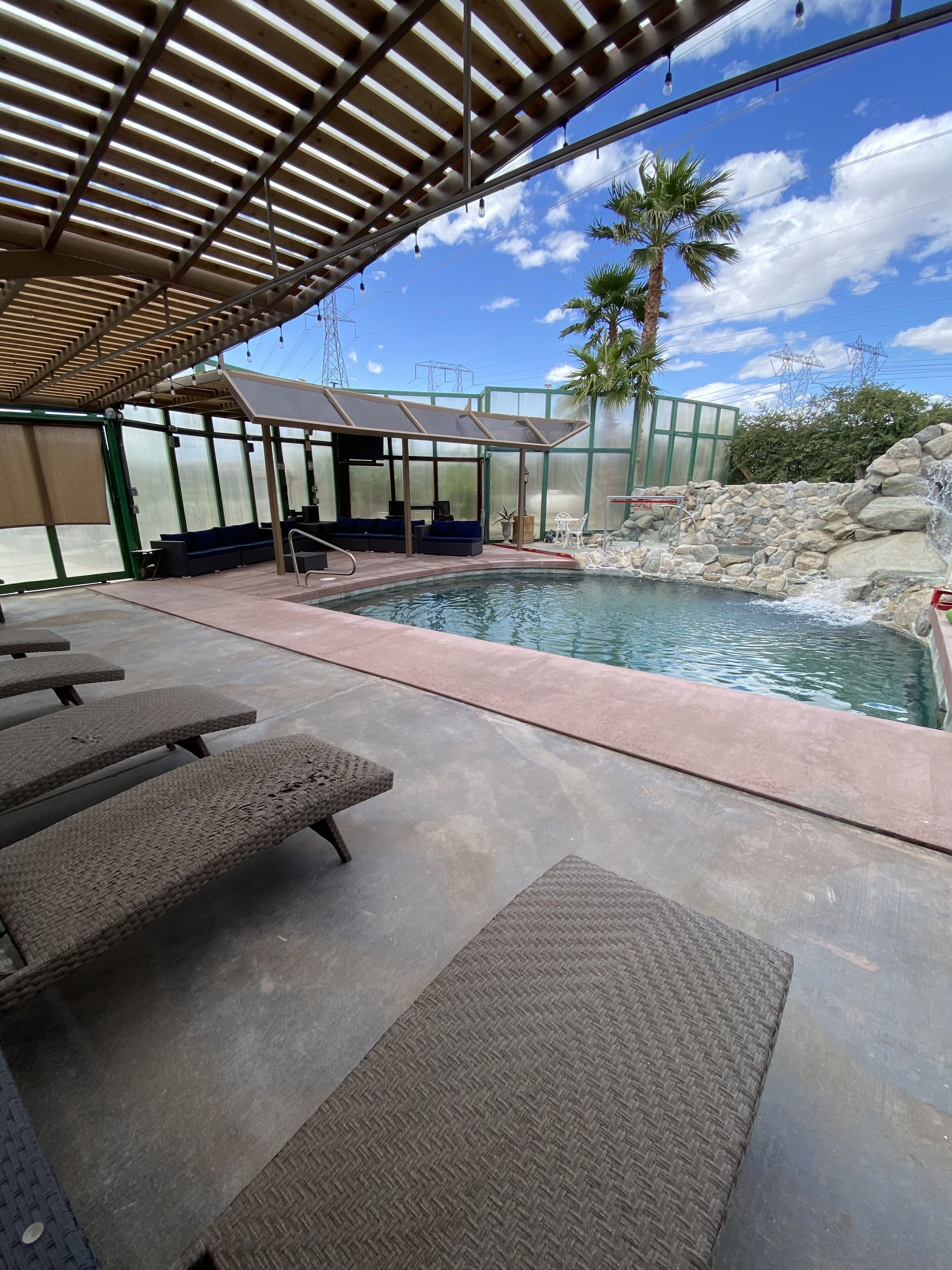 An outdoor pool area with lounge chairs, a covered seating area, and a stone waterfall feature.