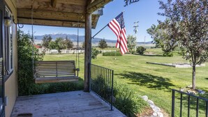 En træterrasse med en bænk, et amerikansk flag og udsigt over en græsmark med bjerge i baggrunden.