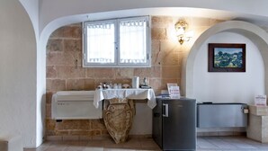 Une cuisine compacte avec un mur en pierre, une fenêtre avec des rideaux, un réfrigérateur et un bouclier décoratif.