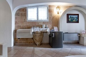 Cozy kitchen with a stone wall, window, and arched doorway, featuring a small refrigerator and decorative urn.
