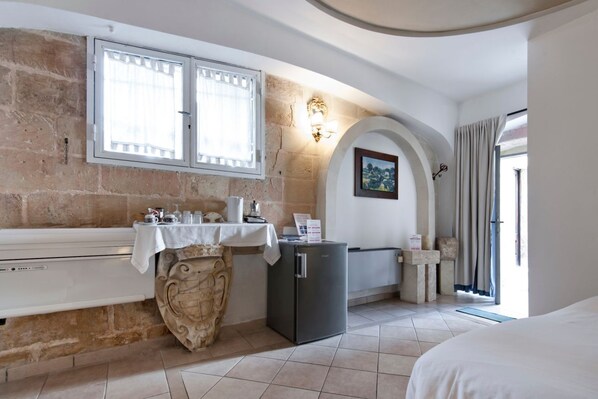 A compact room with a stone wall, a small kitchen area with a refrigerator, a table with kitchenware, and a bed.