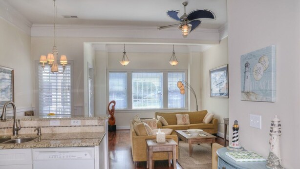 A spacious living room with a sofa, coffee table, and decorative items. A kitchen area with granite countertops and a dishwasher is visible. - Starboard at Captain's Bridge (Southport)