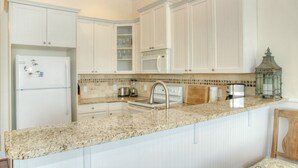 A kitchen with white cabinetry, a granite countertop, a stainless steel sink, and a microwave. - Starboard at Captain's Bridge (Southport)
