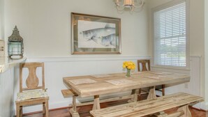 A dining area with a wooden table, chairs, a chandelier, and a framed fish painting on the wall. - Starboard at Captain's Bridge (Southport)
