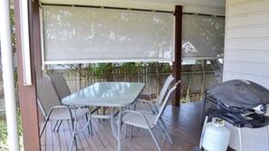 A covered patio with a table and chairs, a grill, and a propane tank.