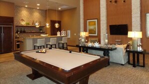 Una mesa de billar en una sala con bar, asientos y una televisión.