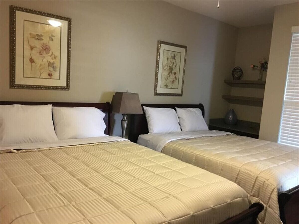 A hotel room with two beds, a nightstand, a lamp, and two framed pictures on the wall.