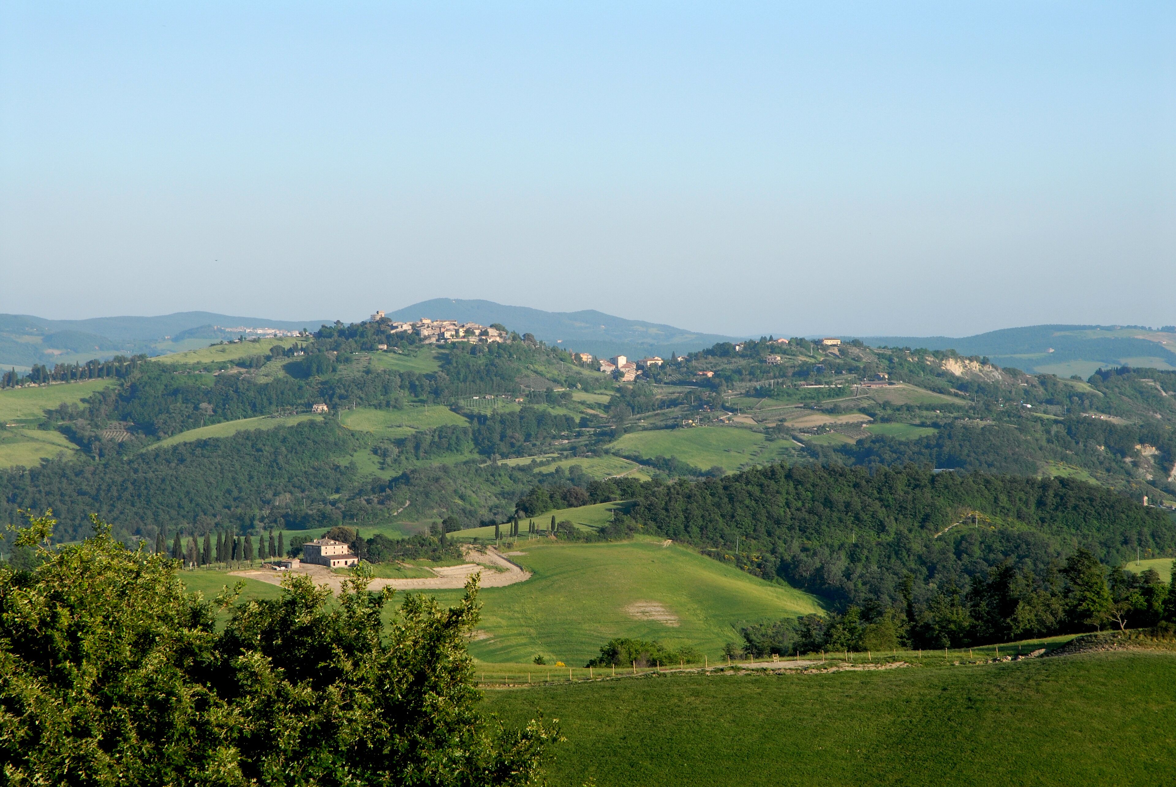 Ein weitreichender Panoramablick über eine hügelige Landschaft mit verstreuten Gebäuden, vermutlich eine ländliche Gegend mit natürlicher Schönheit und historischer Architektur.