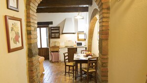 Un couloir étroit, surmonté d’une arche en briques, mène à une salle à manger où se trouvent une table et des chaises.