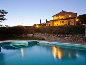 Una casa de piedra con piscina al anochecer.
