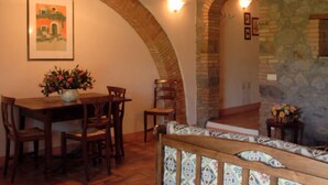 Un coin repas avec une table et des chaises en bois, un vase de fleurs et un mur en pierre agrémenté d’une porte en arc de cercle.