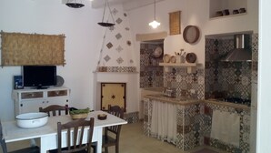 A kitchen with a dining table, chairs, a television, hanging lights, and patterned tiles.