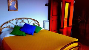 Un letto con copripiumino giallo e due cuscini, testiera in metallo, termosifone e una porta rossa con luce gialla.