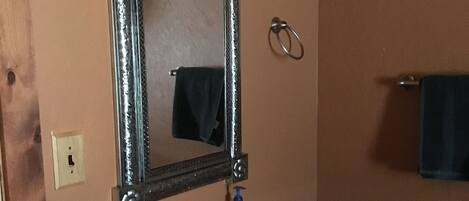 A bathroom with a blue vanity, a mirror with three lights, and a towel ring on the wall.