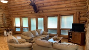 L’intérieur d’une cabane en rondins, avec un canapé en cuir, un téléviseur et une tête de cerf accrochée au mur.