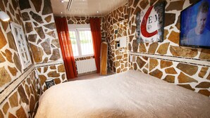 A bedroom with a stone wall, a bed, a television, and a window with curtains. - Finca Casper the high quality natural stone villa by the sea (Els Poblets Alicante)