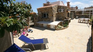 A stone building with a tiled roof, a small patio area with lounge chairs, and a garden with fruit trees. - Finca Casper the high quality natural stone villa by the sea (Els Poblets Alicante)