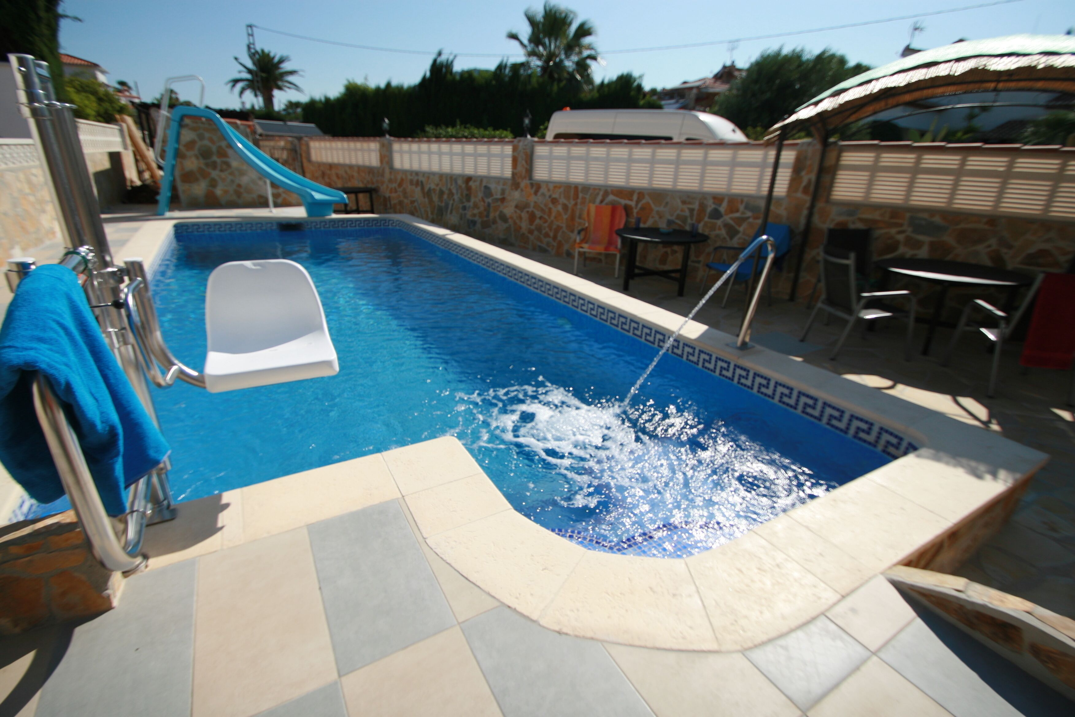 Una piscina con tobogán, escalera y zona de estar con sillas y una mesa.