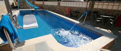 Una piscina con tobogán, escalera y zona de estar con sillas y una mesa.