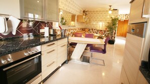 A modern kitchen with a built-in oven, a dining area with a table and chairs, and a refrigerator. - Finca Casper the high quality natural stone villa by the sea (Els Poblets Alicante)