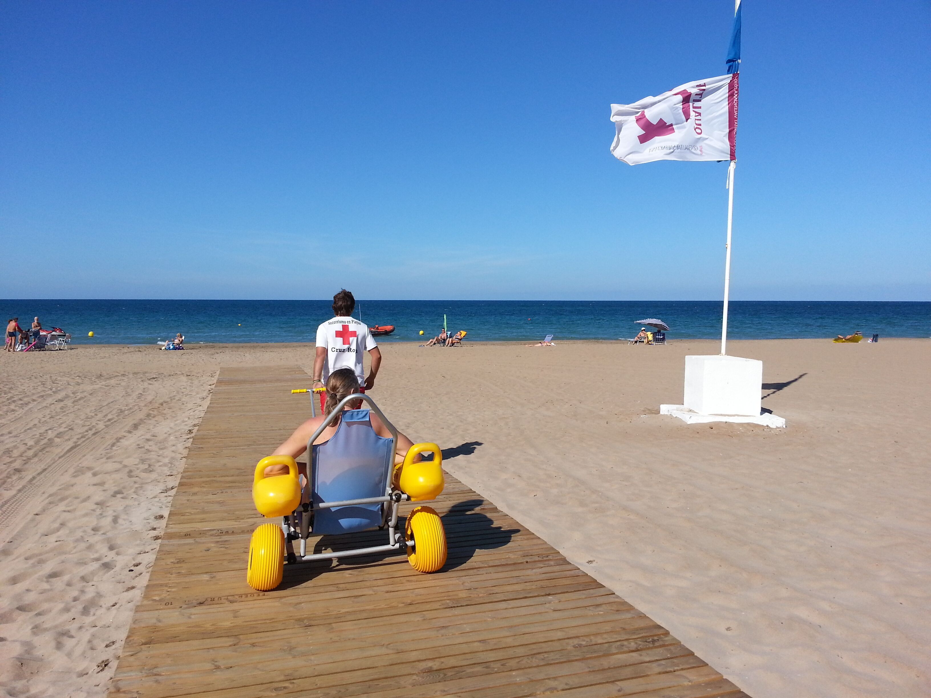 En strandscene med en livredder på en redningsbræt, et flag og en træpromenade.