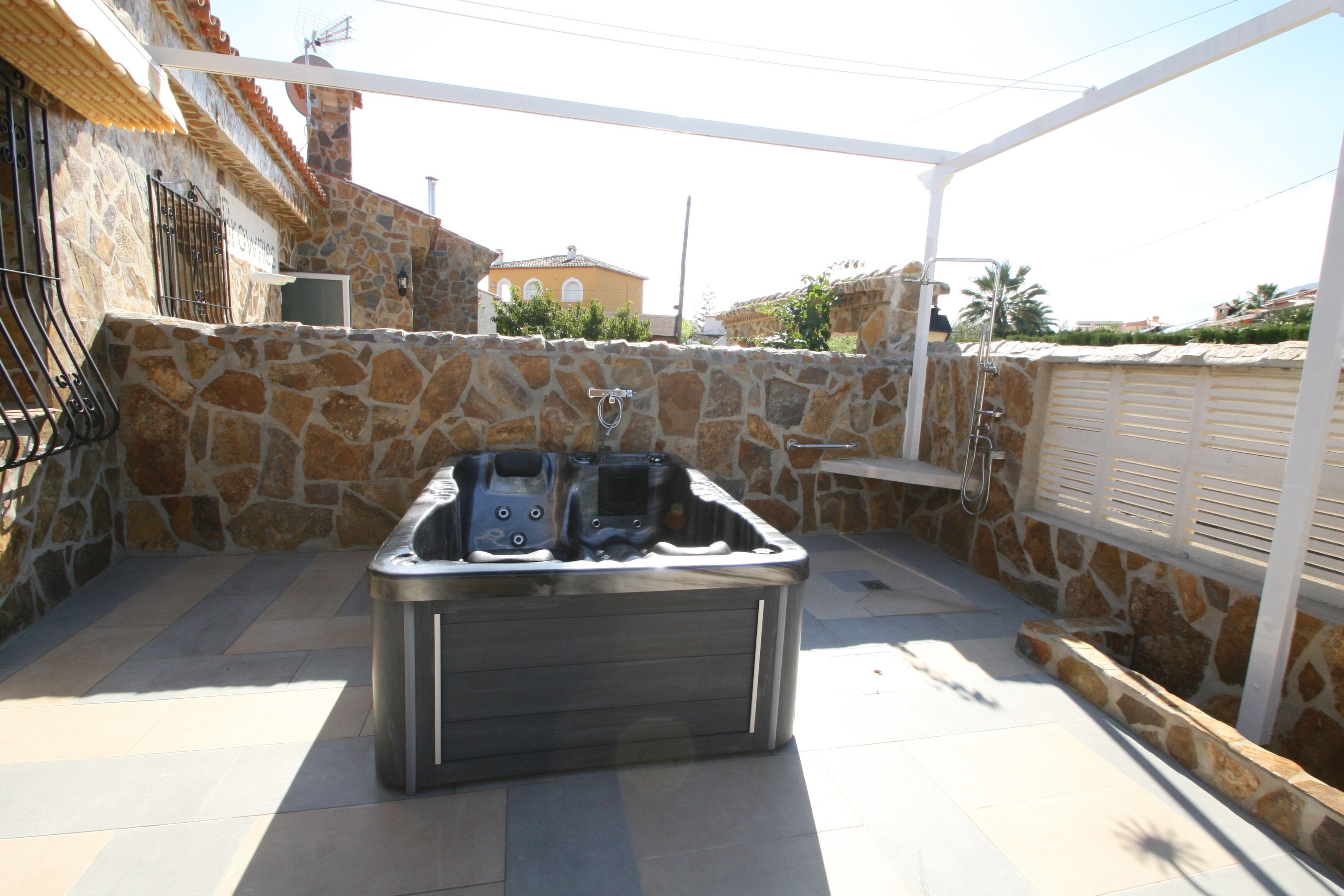 Un bain à remous situé dans un espace extérieur aménagé en patio, avec des murs en pierre et un sol carrelé.