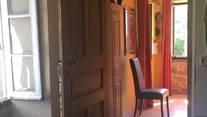 A wooden door leading to a room with a chair and a window with red curtains. - Nice village house (San Andrea di Boziu)