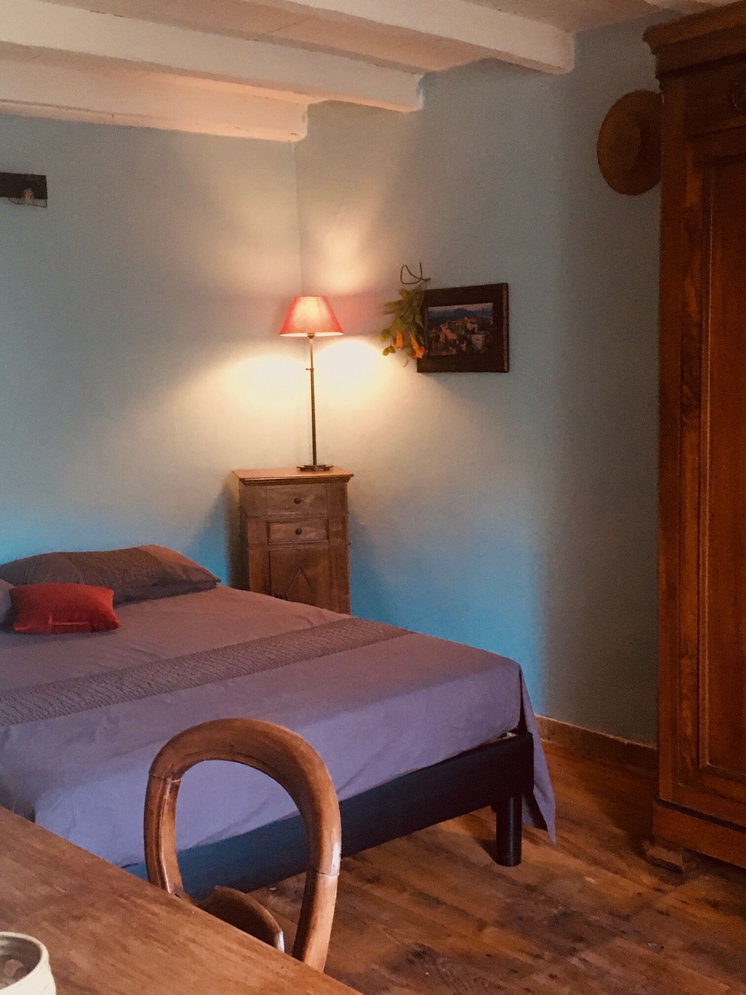 Un dormitorio con cama, una silla de madera, una mesita de noche con lámpara y un armario.