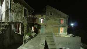 A stone building with a balcony, a staircase, and a small outdoor seating area at night. - Nice village house (San Andrea di Boziu)