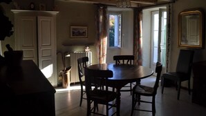 A dining area with a round table and chairs, a kitchen with a radiator, and a window with curtains. - Nice village house (San Andrea di Boziu)